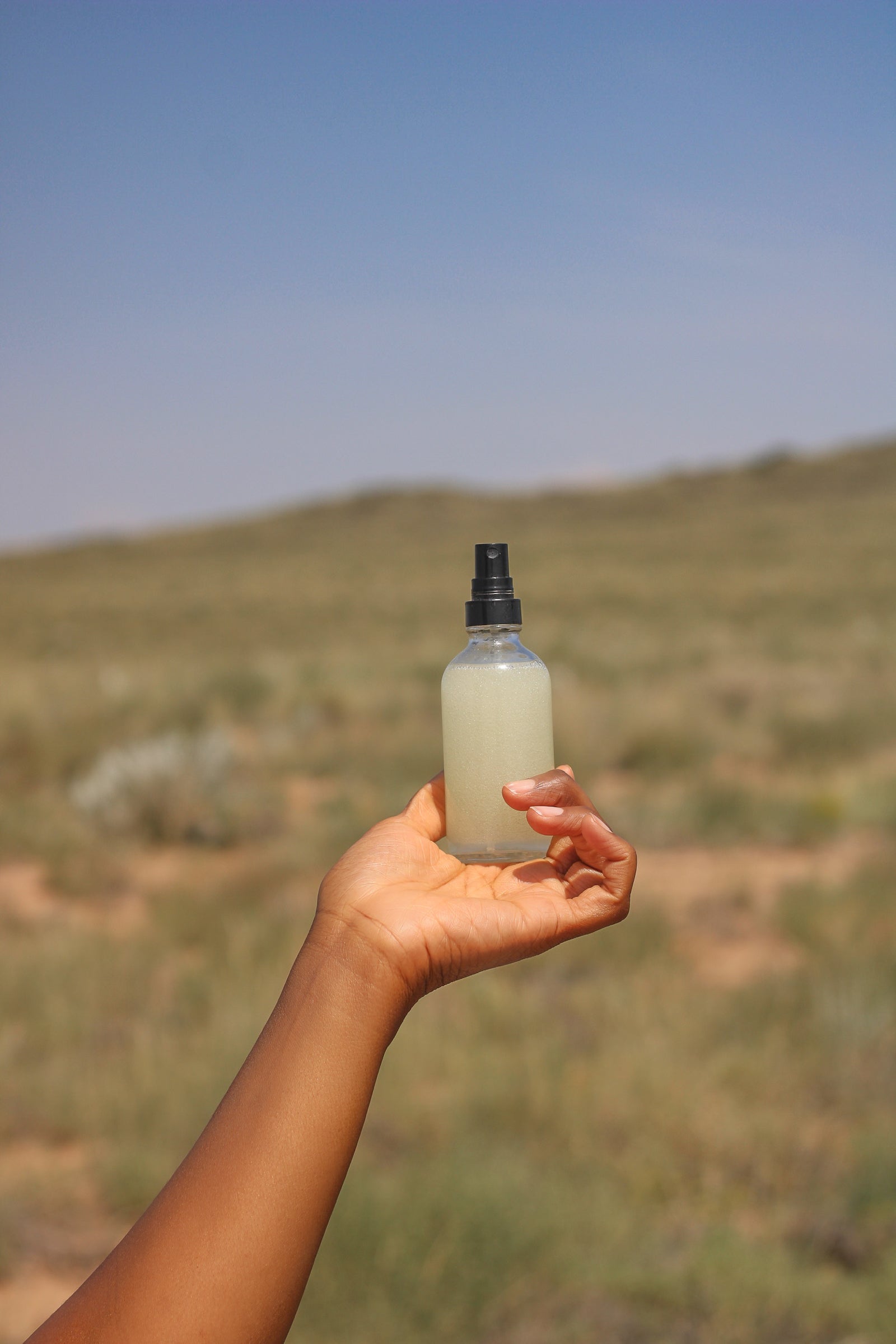 Non-Tacky Mosquito and Gnat Repellant Refreshing Spray in Ayanna's hand with desert and blue sky background