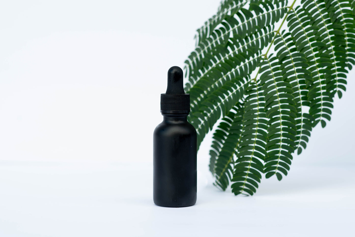 The REAL Skin Serums. plumping, hydrating concentrated  oil in black tincture bottle on white ground and green leaf